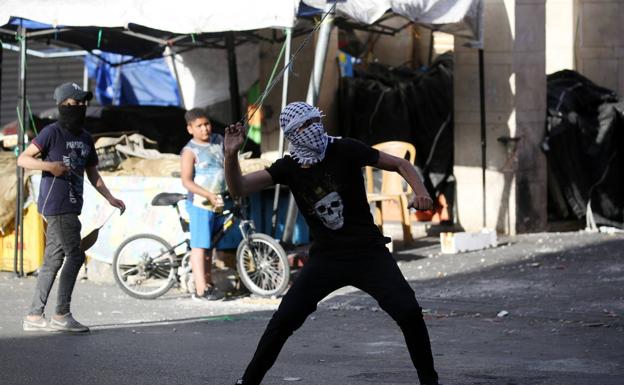 Un palestino arroja una piedra contra soldados israelíes en Hebron.