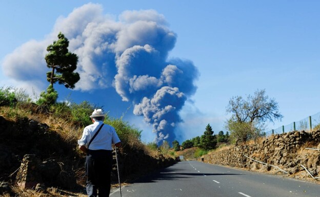 Un hombre camina mientras al fondo se vislumbra la columna de humo y cenizas.  / BORJA SUÁREZ / REUTERS