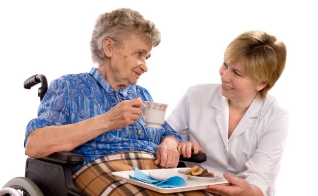 Una anciana recibe la ayuda de una cuidadora. 