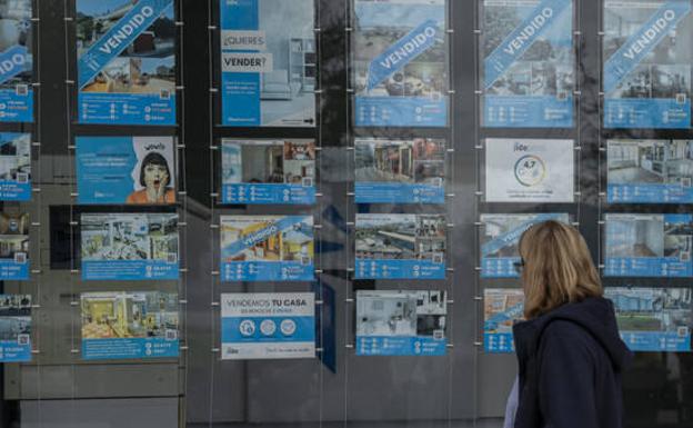 A woman looks at posters of houses for sale in a real estate agency. 