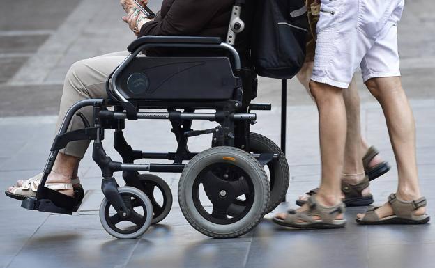 Una persona se desplaza en silla de ruedas con ayuda de familiares. 
