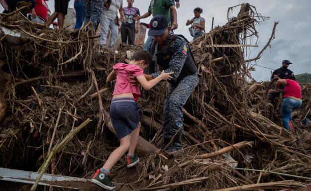 Un policía ayuda a cruzar a un niño en una zona de destrozos en Las Tejerías. /efe